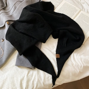 Détail d'une écharpe en maille noire avec étiquette en cuir marron sur fond matelassé