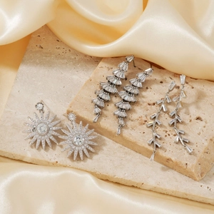 Three pairs of elegant silver sparkling zircon earrings on beige stone and silk background