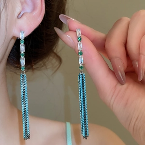 Detail of silver drop earrings with green gemstones and blue tassel chains on model