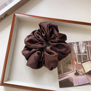 Macro detail of glossy dark brown satin scrunchie on a decorative white wooden tray