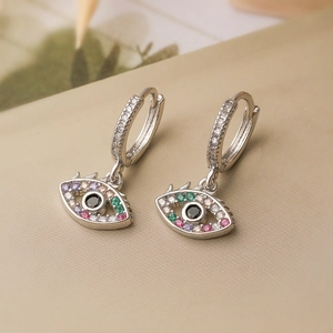 Delicate silver evil eye hoop earrings with colorful cubic zirconia on beige fabric