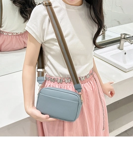 Blue crossbody bag with lychee texture and striped wide strap shown on a female model
