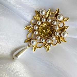 Detail of vintage gold brooch with Elizabeth II coin, pearls and leaf accents on white silk