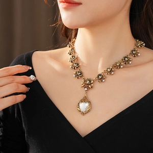 Détail d'un collier vintage doré avec fleurs, strass et pendentif perle sur un mannequin