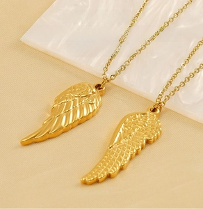 Close-up of golden stainless steel angel wing pendants on a soft fabric background