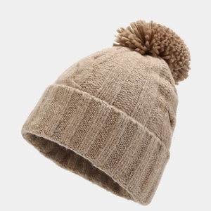 Close-up of thick cable knit pattern and large faux fur pom-pom on beige winter beanie