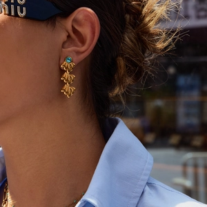 Close-up of golden leaf drop earrings with a blue gemstone on a female model