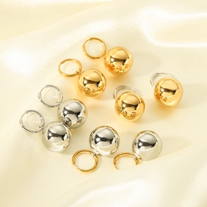 Polished 18K gold and silver hollow ball drop earrings on soft beige silk background
