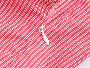Close-up of a white invisible zipper with a teardrop metal pull on a red striped fabric