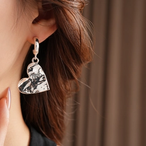 Detailed close-up of textured heart-shaped silver pendant earring worn by a model