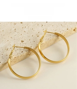 Close-up of large gold-plated hoop earrings with clasp on a natural stone base