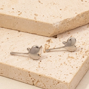 Polished 304 stainless steel heart-shaped studs displayed on minimalist beige stone props