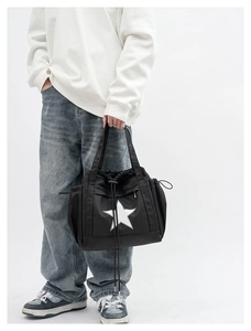 Detail of black crossbody bag with white star logo carried by model in casual outfit