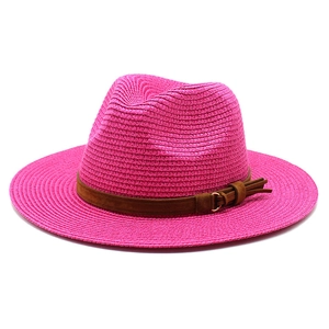 Detail of rose pink straw sun hat featuring brown faux leather band with tassel and buckle