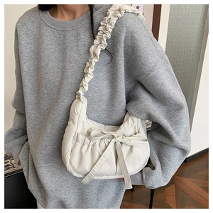 Detail of creamy white quilted puff bag with bow decoration and pleated shoulder strap