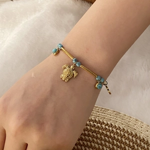 Golden sea turtle bracelet with turquoise beads on a wrist against a beach-style background