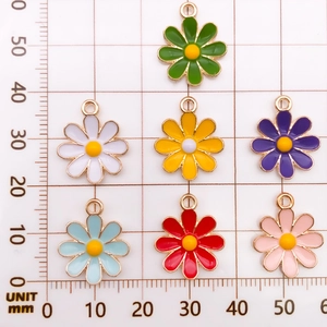 Flat lay of colorful daisy flower alloy charms with measurement grid for DIY jewelry