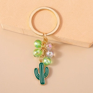 Close-up of golden cactus keychain with green beads and iridescent chain on beige surface