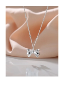 Detail of s925 silver bow necklace featuring bead chain on soft pink silk background