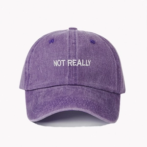 Detailed close-up of white NOT REALLY embroidery on purple washed denim baseball cap