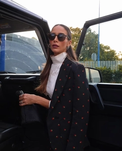 Détail de la broderie fraise sur un blazer noir avec un haut blanc à col roulé froncé