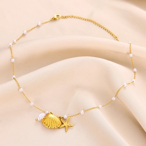 Gold ocean necklace with seashell, starfish, and white pearl charms on silk fabric