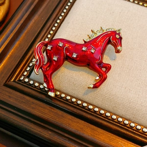Close-up of vintage gold horse brooch with red enamel and shimmering diamond accents