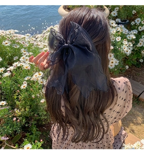 Detail of a large black sheer mesh bow hair clip worn by a girl on long hair outdoors