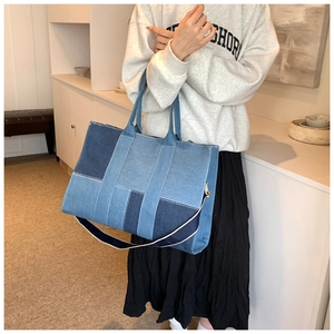 Detail of large denim tote bag featuring blue patchwork design and woven shoulder strap
