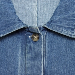 Nahaufnahme eines blauen Jeanshemdes mit spitzem Kragen und hochwertigem dunklem Knopf