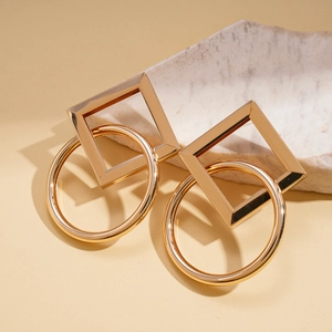 Detail view of gold geometric earrings with square and circle frames on marble stone