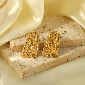Détail de boucles d'oreilles en acier titane doré avec texture lave sur socle