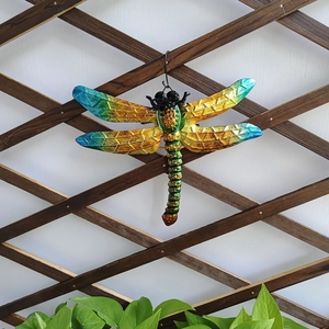 Detailed view of hand-painted metal dragonfly wall decor on wooden lattice background