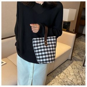 Detail of checkered canvas bucket bag with brown leather handle in a lifestyle setting