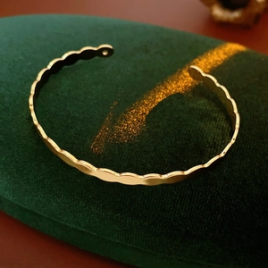 Detail shot of a golden wavy twisted open bangle on a green velvet display stand