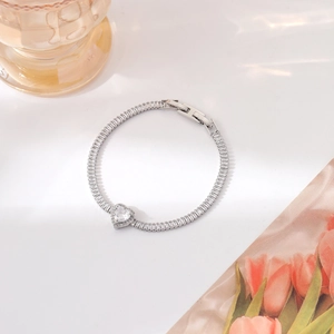 Detailed macro view of silver sparkling zircon bracelet with heart pendant on white surface