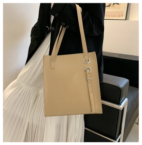 Detail shot of a large beige leather tote bag with metal buckle on a shoulder model