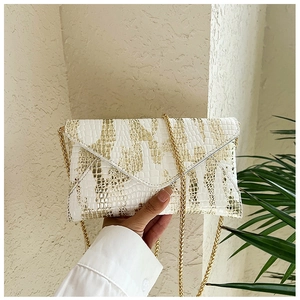 Detailed view of crocodile pattern envelope bag with gold chain strap and metal trim