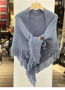 Close-up of soft blue knit shawl with tassel edge detailing on a wooden hanger