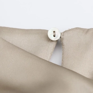 Vue détaillée du bouton nacré et du tissu satiné soyeux de couleur doré champagne