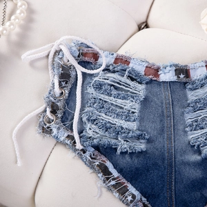 Dettaglio di pantaloncini in denim a vita bassa con lacci laterali e strappi vintage