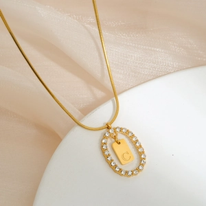 Macro shot of gold oval pendant with micro-inlaid rhinestones and letter C engraving