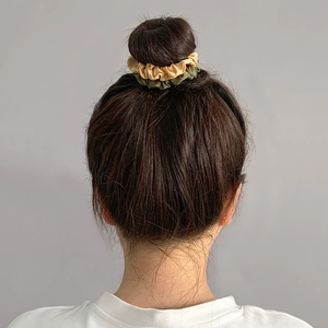 Close-up of beige and olive green satin scrunchies styling a messy bun on a woman