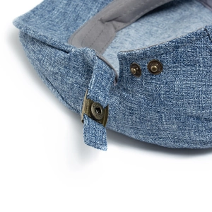 Close-up of light blue linen-textured beret hat with adjustable bronze metal buckles