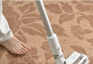 Detail of a white handheld vacuum cleaner with an orange roller brush cleaning a floral rug