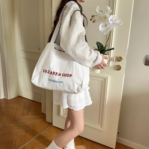 Nahaufnahme einer weißen Canvas-Tasche mit roter Stickerei und gestreiftem Gurt