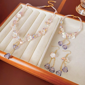 Detailed set of purple crystal flower necklace, bracelet and earrings in a beige tray