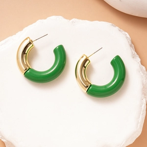 Detail of C-shaped earrings with green acrylic and gold metal on a white stone