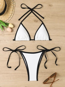 Detailed flat lay of white bikini with black trim and wavy textured fabric on wood