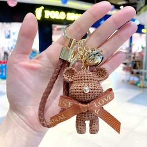 Close-up of brown textured resin bear keychain with golden bell and ribbon detail